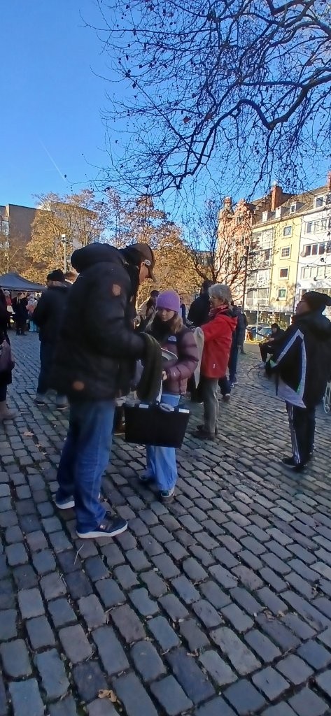 Menschen in Winterkleidung treffen sich auf einem gepflasterten Platz in Aachen.