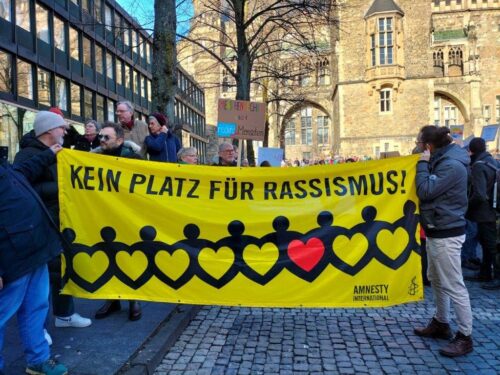 Menschen halten bei einer Demo auf dem Aachener Katschhof ein Amnesty-Banner mit Aufschrift "Kein Platz für Rassismus!"