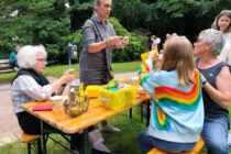 An einer Bierzeltgarnitur im Aachener Stadtpark zeigen Teilnehmer*innen des Strickcafés verschiedene Techniken. OB Sybille Keupen schaut vorbei.